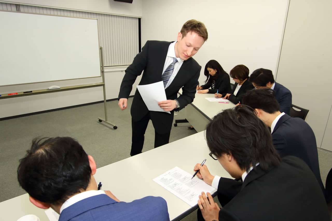 先生はビジネス英会話のクラスで生徒が書いている様子をチェックし、進捗をみています